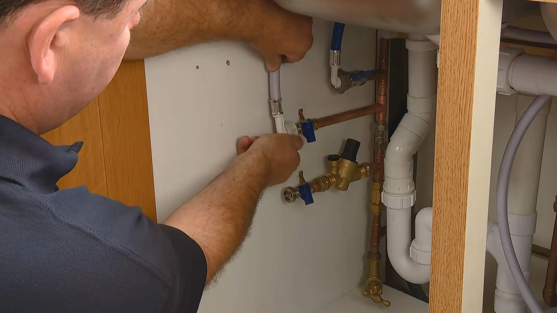 Man in a dark shirt working at the supply valves inside a sink cabinet