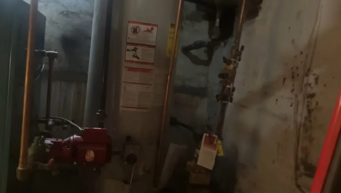 Utility room wall with copper and steel pipes running past a red pump and warning labels